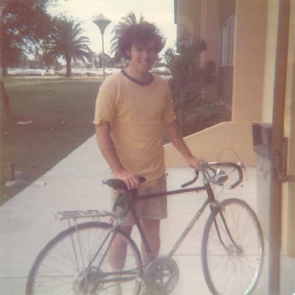 Older photo of alumnus Mike Murphy standing next to his bike outside of McKay